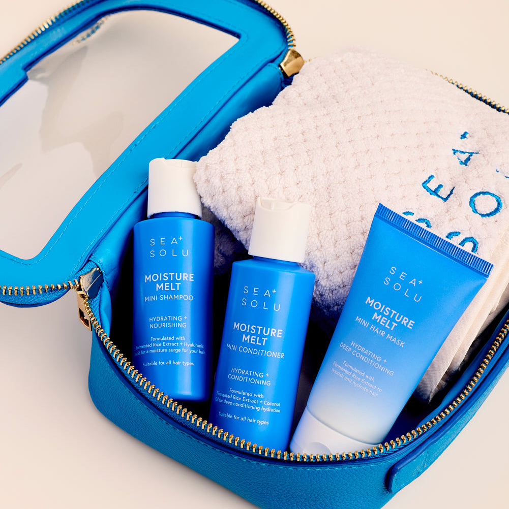 A bright blue zippered toiletry bag opened on a light beige background, containing three Sea Solu Moisture Melts bottles and a white textured towel.